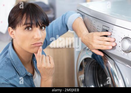 une femme contrariée assise devant un lave-linge endommagé Banque D'Images