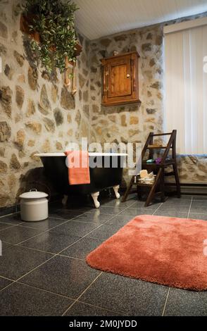 Baignoire avec pied à griffe noir et blanc et mobilier ancien dans la salle de bains à l'intérieur d'une réplique de l'ancienne maison de style cottage Canadiana en bois et pierre de champ. Banque D'Images