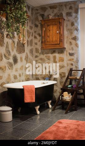 Baignoire avec pied à griffe noir et blanc et mobilier ancien dans la salle de bains à l'intérieur d'une réplique de l'ancienne maison de style cottage Canadiana en bois et pierre de champ. Banque D'Images