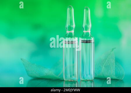 Ampoules et feuilles vertes squelettes sur fond turquoise vert flou.sérum de mésothérapie et de dermabrasion en ampoules.acide hyaluronique en Banque D'Images