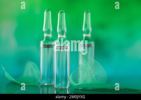 Ampoules cosmétiques.produits de beauté.ampoules transparentes et feuilles vertes squelettes sur fond turquoise vert flou.Mésothérapie et Banque D'Images