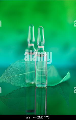 Ampoules cosmétiques et feuilles vertes squelettes sur fond turquoise vert flou.sérum de mésothérapie et de dermabrasion en ampoules.acide hyaluronique Banque D'Images