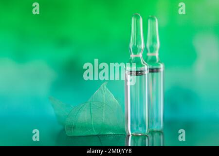 Produits de beauté.ampoules transparentes et feuilles vertes squelettes sur fond turquoise vert flou.sérum de mésothérapie et dermabrasion Banque D'Images