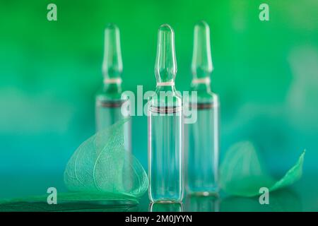 Acide hyaluronique en ampoules.ampoules cosmétiques.produits de beauté.ampoules transparentes et feuilles vertes squelettes sur fond turquoise flou Banque D'Images