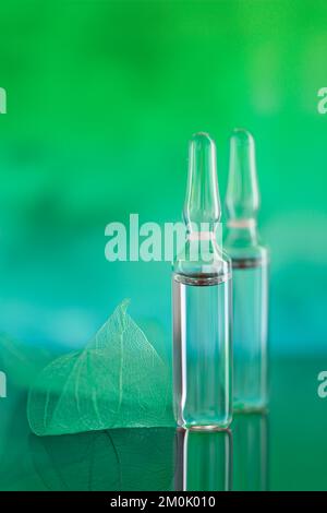 Ampoules transparentes et feuilles vertes squelettes sur fond turquoise vert flou.sérum de mésothérapie et de dermabrasion en ampoules.Hyaluronic Banque D'Images