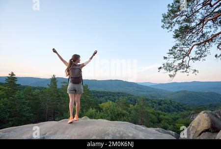 Une randonneur se tenant sur un sentier de randonnée en montagne levant les mains en profitant de la nature du soir pendant son voyage sur un sentier sauvage. Voyageur solitaire Banque D'Images