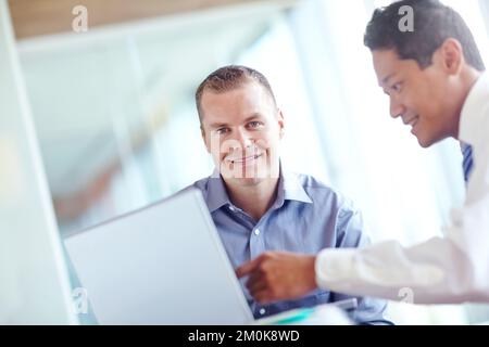 Nous sommes heureux de recevoir les meilleurs conseils. Deux jeunes hommes d'affaires travaillent ensemble tout en partageant un ordinateur portable entre eux. Banque D'Images