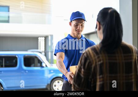 Un livreur professionnel en uniforme bleu qui remet le colis au client en se tenant devant sa camionnette Banque D'Images