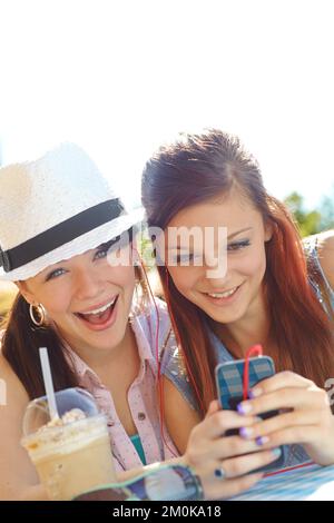 Découvrir de nouveaux groupes ensemble. Deux adolescentes partageant des écouteurs tout en écoutant de la musique sur un téléphone portable. Banque D'Images