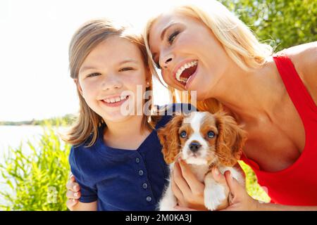 Mamans les meilleures. Portrait d'une petite fille tenant un chiot tandis que sa mère lui sourit avec amour. Banque D'Images