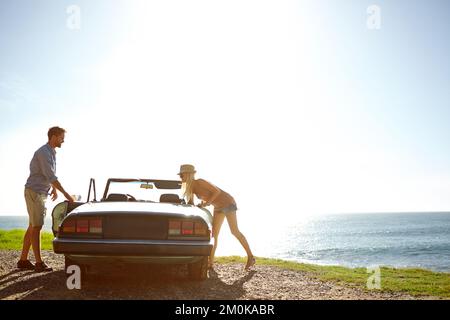 S'arrêter pour étirer les jambes. Un jeune couple garé au bord de l'océan debout près de leur convertible. Banque D'Images