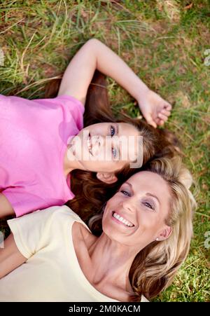 La mielle a obtenu un lien étroit. Une mère heureuse et sa jeune fille couchée sur l'herbe ensemble à l'extérieur et regardant vers le haut. Banque D'Images