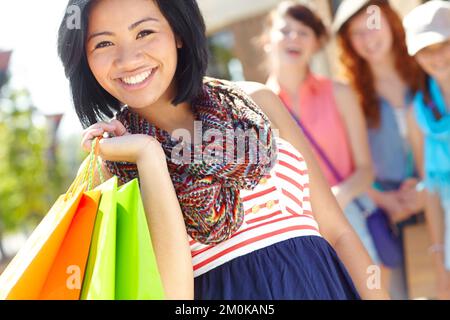 Satisfait de ses achats. Une belle fille ethnique tenant des sacs de shopping et souriant avec ses amis en arrière-plan. Banque D'Images