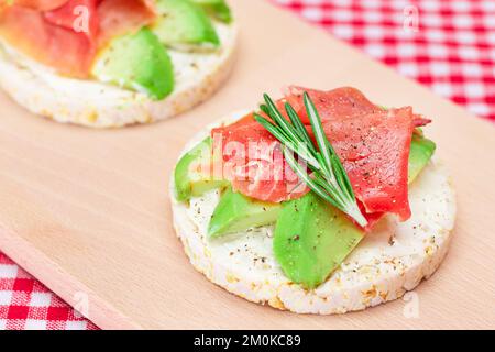 Sandwich au gâteau de riz avec avocat, Jamon, olives et romarin sur planche à découper en bois. Petit déjeuner facile. Sandwichs rapides et sains. Croustillant et garniture savoureuse. En-cas diététiques Banque D'Images