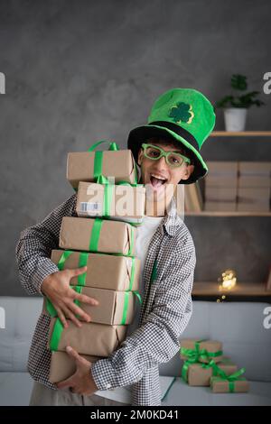 Excitée drôle arabe homme porte leprechaun chapeau regardant l'appareil photo tenant beaucoup de boîtes cadeaux célébrant St.Patricks jour. Présente les soldes de magasinage sur St.Pat Banque D'Images