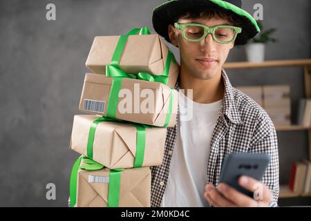 St patrick's Day sale, commerçant en ligne en chapeau de lepreun vert avec pile de boîtes cadeaux à l'aide d'un smartphone. Portrait Banque D'Images