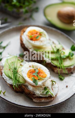 Pain grillé, œufs durs, tranche d'avocat, micro-légumes sur une assiette, heure du petit déjeuner Banque D'Images