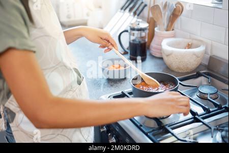 Gros plan des mains de femmes préparant la nourriture sur la cuisinière dans la cuisine à la maison. Femme méconnaissable tenant une cuillère et remuant la sauce pendant la cuisson Banque D'Images