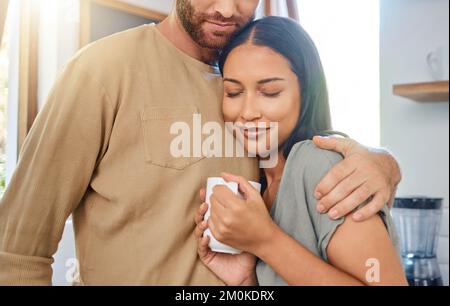 Un jeune couple interracial aimant passe du temps ensemble à la maison. Jeune femme appréciant son café du matin tandis que l'ami met ses bras autour d'elle Banque D'Images