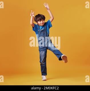 Un enfant de race mixte mignon portant des vêtements décontractés tout en s'amusant et en étant énergique contre un arrière-plan d'imitation orange. Enfant asiatique actif Banque D'Images