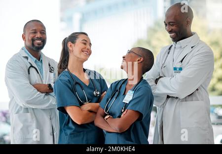 Groupe de médecins et d'infirmières heureux debout en ligne avec leurs bras croisés tout en travaillant dans un hôpital. Professionnels de la santé gaies Banque D'Images