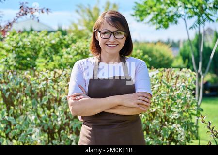 Portrait d'extérieur une femme souriante jardinière regardant l'appareil photo dans l'arrière-cour Banque D'Images
