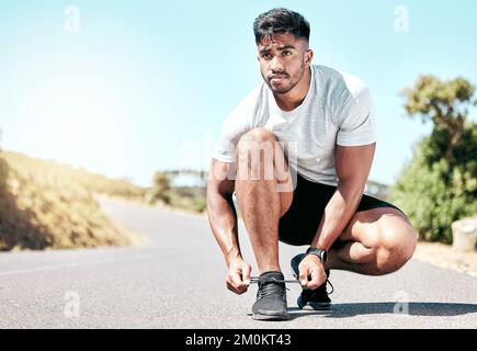 Jeune sportif mixte homme de course nouant ses lacets avant une course. Beau athlète hispanique masculin fixant ses lacets et se préparer pour une course Banque D'Images