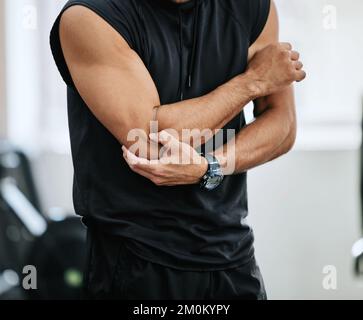 Entraîneur inconnu seul dans la salle de gym et souffrant de blessures de coude. Un entraîneur debout et bras de frottement pendant l'entraînement dans le club de santé d'exercice. Un homme dedans Banque D'Images