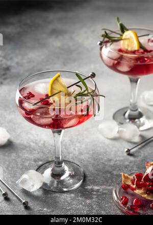 Deux verres de cocktail glacé de Noël à la grenade avec romarin et citron sur fond gris. Boisson de fête de Noël. Orientation verticale Banque D'Images