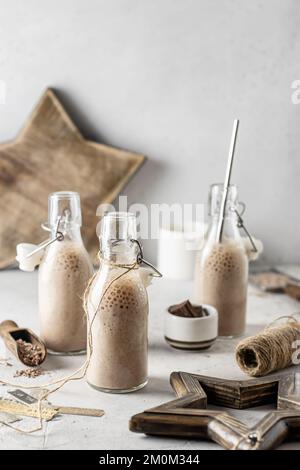 Milk-shakes au chocolat dans des bouteilles en verre avec décoration de noël sur fond blanc texturé. Ambiance de Noël, Noël festif encore vie. Orientation verticale Banque D'Images
