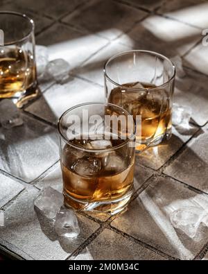 Whisky avec glace dans des verres. Fond de mosaïque gris. Lumière dure, espace de copie. Orientation verticale Banque D'Images