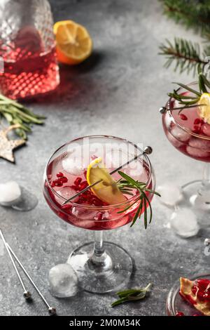 Deux verres de cocktail glacé de Noël à la grenade avec romarin et citron sur fond gris. Boisson de fête de Noël. Orientation verticale Banque D'Images