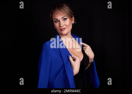 une femme adulte caucasienne a jeté une veste bleue sur ses épaules sur un fond noir. Photo de haute qualité Banque D'Images