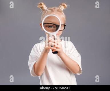 curieuse petite fille caucasienne tenant et regardant à travers une loupe sur fond neutre Banque D'Images