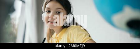 fille souriante regardant l'appareil photo tout en écoutant de la musique dans le casque, la bannière Banque D'Images