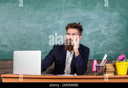 Je suis votre nouveau professeur. Enseignant prêt à commencer la leçon. Un professeur s'assoit au bureau avec un ordinateur portable. Concept de retour à l'école. Boxer à barbe avec professeur Banque D'Images