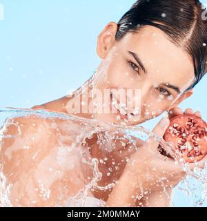 Portrait, douche et grenade avec une femme modèle en studio sur fond bleu pour la santé, l'hygiène ou l'hydratation. Eau, éclaboussures et fruits avec Banque D'Images