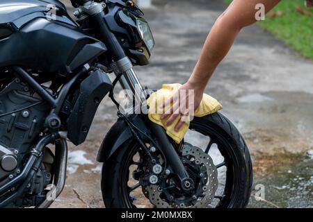Jeune homme motard nettoyant et lavant sa moto devant la maison. Banque D'Images