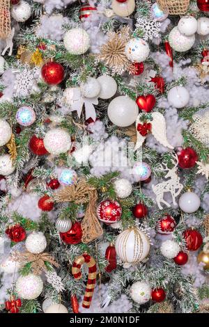 Nouvel an et arrière-plan de Noël. Sapin de Noël recouvert de neige décoré de décorations de Noël suspendues boules rouges et blanches, anges, cannes de bonbons, Banque D'Images