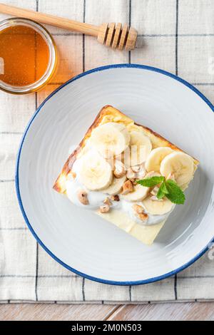 Une tranche de gâteau au fromage cottage est servie avec du yaourt, des tranches de banane, du miel et des noix hachées. Un petit-déjeuner sucré et sain Banque D'Images