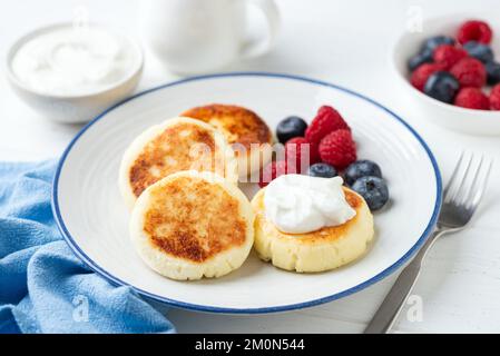 Beignets de fromage cottage sucré, le Syrniki est servi avec des baies et du yaourt grec. Dessert ou nourriture saine pour le petit déjeuner Banque D'Images