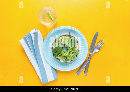 Petit déjeuner végétalien sain, pain grillé à l'avocat avec des micro-légumes et un verre d'eau sur fond jaune. Repas de régime. Vue de dessus Banque D'Images