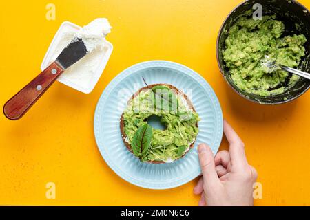 Petit déjeuner bagel toast avec fromage à la crème, avocat, vert sur fond jaune. Plaque de maintien pour hommes avec pain grillé à l'avocat Banque D'Images