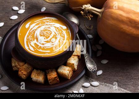 Soupe de potiron à la crème et aux graines de sésame dans un bol en céramique marron sur fond de bois Banque D'Images