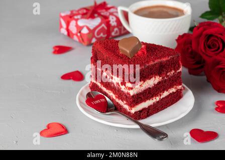 Un morceau de gâteau de velours rouge, une tasse de café, des roses et un cadeau pour la Saint Valentin sur fond gris clair Banque D'Images