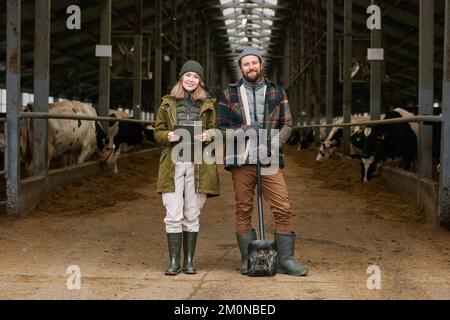 Portrait de deux agronomes souriant à la caméra travaillant avec un Tablet pc et une bêche dans un abri de vache Banque D'Images