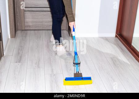 Une femme lave le sol stratifié dans l'appartement avec une vadrouille. Nettoyage de la maison. Banque D'Images