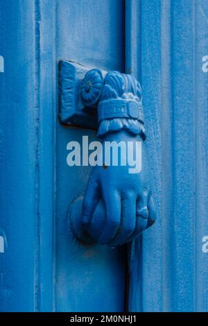 Vue rapprochée de l'élégant knocker de porte en laiton vintage en forme de main tenant la boule isolée sur la porte en bois bleu clair, Montpellier, France Banque D'Images