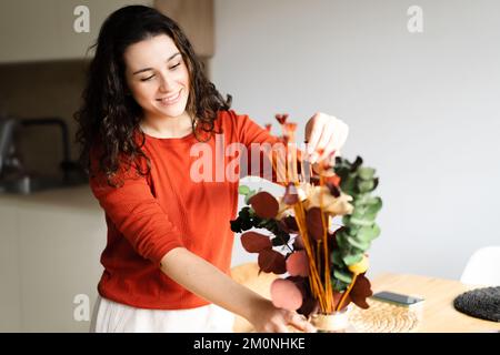 Jeune femme heureuse organisant des fleurs séchées dans un vase et plaçant la table dans la cuisine Banque D'Images