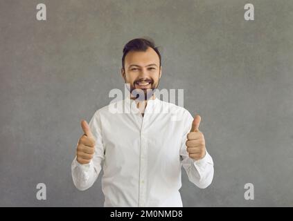Portrait d'un jeune homme heureux donnant des pouces debout isolé sur fond gris Banque D'Images